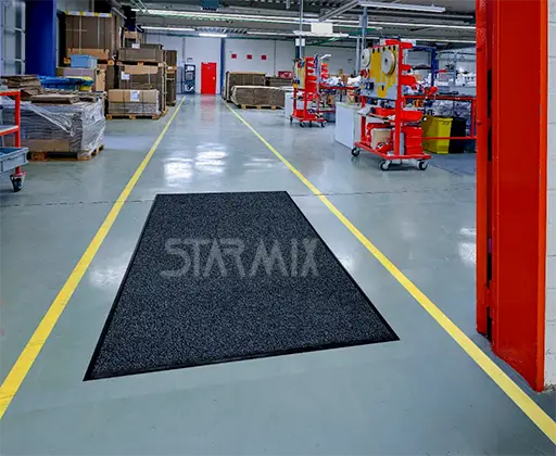 Tapete absorvente industrial de grande formato instalado em corredor de indústria para contenção de umidade e sujeira.