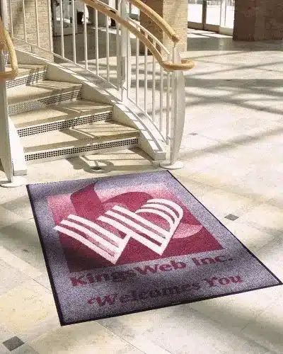Tapete personalizado de alto padrão para recepção de hotel com logomarca KingsWeb Inc, posicionado próximo a uma escadaria elegante.